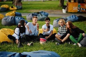 Young multi ethnic group of people watching movie at poof in open air cinema and making selfie on phone. photo