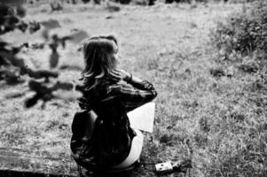 retrato de una joven y hermosa rubia positiva sentada en el suelo con un mapa en las manos en el bosque. foto