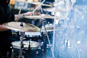 el baterista toca la batería en el escenario en una sala de conciertos detrás de una pared de vidrio. foto