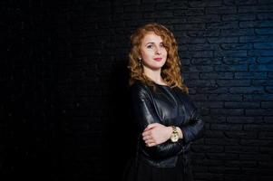 Curly hair girl at leather jacket on studio against black brick wall. photo