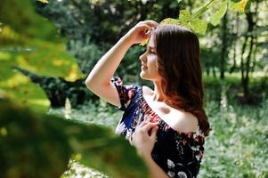 Close-up portrait of a beautiful brunette in dress next to the leaves. photo