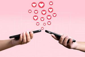 People use mobile phone sending heart to each other. Love and connection concept using telephone application on pink background. photo