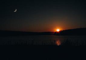 anochecer sobre un lago con luna y sol foto