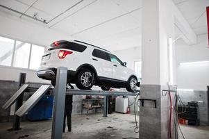 coche todoterreno americano en soporte para verificación de inclinación de alineación de ruedas en el taller de la estación de servicio. foto