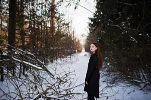 Fashionable long legs brunette model in long black cloak posed outdoor at winter day. photo