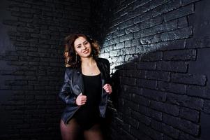 Studio portrait of sexy brunette girl in black leather jacket against brick wall. photo