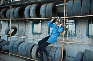 Young hipster girl in jeans jacket and head scarf at tire fitting zone. photo