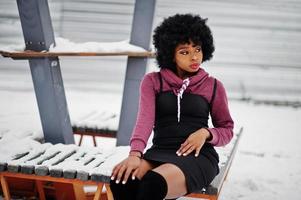 Curly hair african american woman posed at winter day, sitting on bench. photo