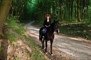 chica mística en ropa de corona en negro a caballo en madera. foto