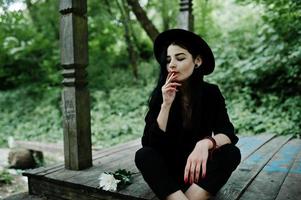 Sensual smoker girl all in black, red lips and hat. Goth dramatic woman smoking thin cigarette. photo