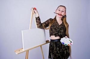 Beautiful woman artist painter with brushes and oil canvas posing in studio isolated on white. photo