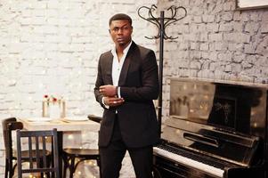 Strong powerful african american man in black suit standing against piano. photo