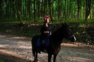 chica mística en ropa de corona en negro a caballo en madera. foto