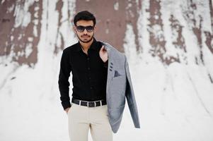 Casual young indian man in black shirt and sunglasses with jacket on shoulders posed at winter day. photo