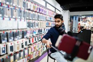 Indian man customer buyer at mobile phone store making selfie by smartphone on monopod stick. South asian peoples and technologies concept. Cellphone shop. photo