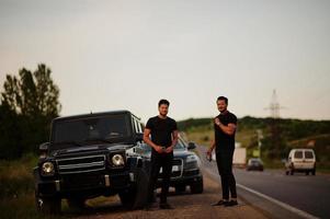 dos hermanos asiáticos se visten de negro y posan cerca de los autos todoterreno. foto