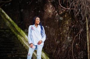 elegante chica afroamericana con rastas sosteniendo el teléfono móvil a mano, clima nevado al aire libre. foto