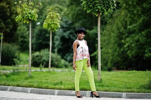 increíble mujer modelo afroamericana en pantalones verdes y sombrero negro posó en el parque. foto