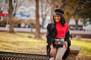 African american fashion girl in coat and newsboy cap posed at street. photo
