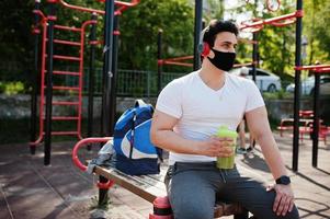 Portrait sports arabian man in black medical face mask posed outdoor with earphones during coronavirus quarantine. photo