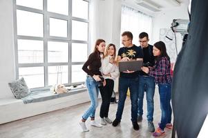 Photographer explaining about the shot to his team in the studio and looking on laptop. Talking to his assistants holding a camera during a photo shoot. Teamwork and brainstorm.