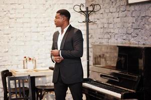 Strong powerful african american man in black suit standing against piano. photo