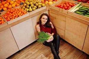 chica de rojo con cebollas verdes en la tienda de frutas. foto