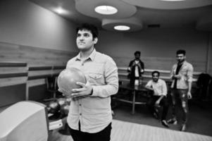 South asian man in jeans shirt standing at bowling alley with ball on hands. Guy is preparing for a throw. photo