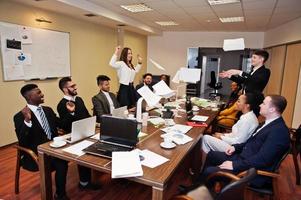 Multiracial business team meeting around boardroom table, two team leaders throw paper up. photo