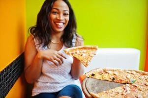 African woman with pizza sitting at bright colored restaurant. photo