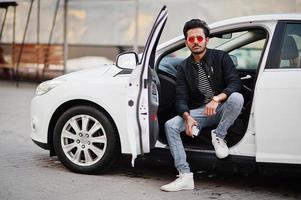 South asian man or indian male wear red eyeglasses sitting inside his white transportation car. photo