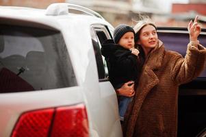 la joven madre y el niño se paran cerca de su auto todoterreno. concepto de conducción segura. foto