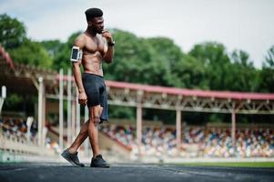 African american male athlete sexy sport bare torso man with running sports arm case for mobile phone, posed at stadium. photo