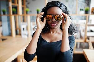 cerrar la cara de una chica afroamericana con gafas de sol posadas en un café moderno. foto