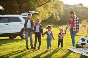 Family spending time together. Mother with four kids standing and holding hands against white suv car. photo