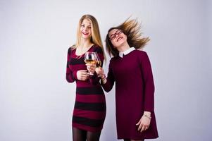 Two attractive friends in purple dresses drink sparkling wine or champagne in the studio. photo