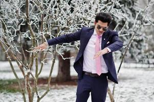 Elegant indian macho man model on suit and pink tie, sunglasses posed on winter day shows dab. photo