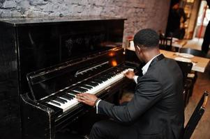 la parte posterior de un hombre afroamericano fuerte y poderoso con traje negro toca el piano. foto