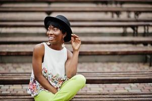 increíble mujer modelo afroamericana en pantalones verdes y sombrero negro posó en el banco. foto