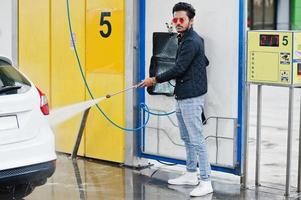 South asian man or indian male washing his white transportation on car wash. photo