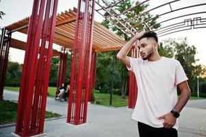 hombre de barba india con estilo en camiseta rosa. modelo india posó bajo un arco rojo en el parque de la ciudad. foto