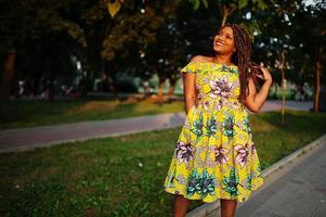 Cute small height african american girl with dreadlocks, wear at coloured yellow dress, posed at sunset. photo