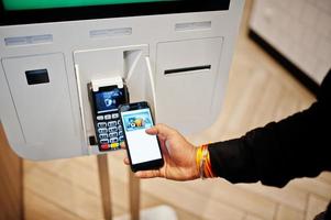 Hands of man customer at store place orders and pay by contactless credit card on mobile phone through self pay floor kiosk for fast food, payment terminal. Pay pass. photo