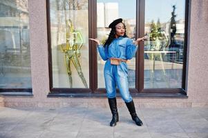 Stylish fashionable african american women in jeans wear and black beret against modern building with three golden mannequins. photo