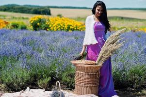 hermosa niña india usa vestido tradicional saree india en campo de lavanda púrpura con canasta. foto