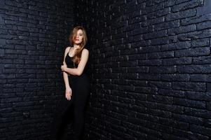 Handsome brunette girl wear on black, posing at studio against dark brick wall. Studio model portrait. photo