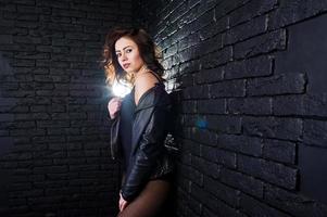 Studio portrait of sexy brunette girl in black leather jacket against brick wall. photo