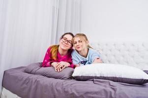 Two friends girls in pajamas having fun on bed at room. photo