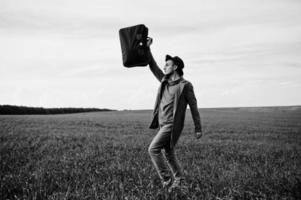 Stylish man in glasses, brown jacket and hat with bag posed on green field. photo