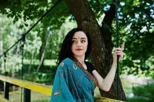 Portrait of beautiful indian brumette girl or hindu woman model on bridge. Traditional Indian costume lehenga choli. photo